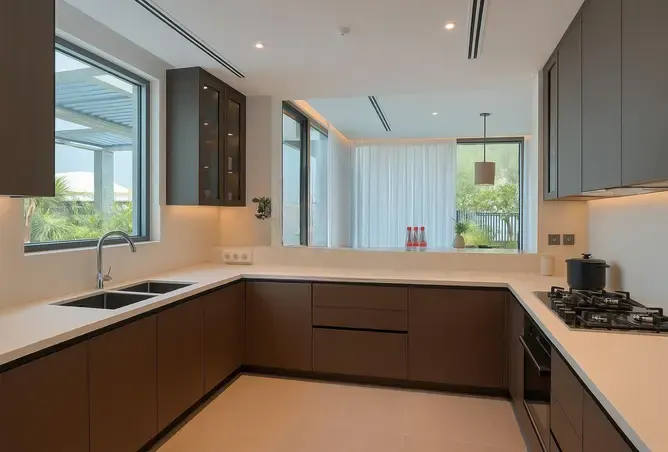 Modern kitchen with brown cabinets, white countertops, and stainless steel appliances. A window overlooks a lush green landscape.