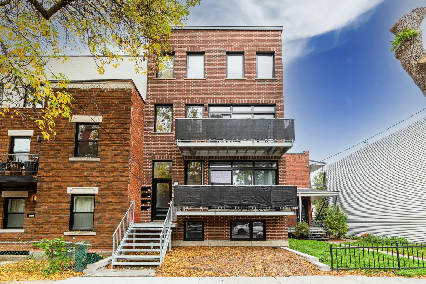 A three-story brick apartment building with two balconies and metal stairs leading to the entrance.