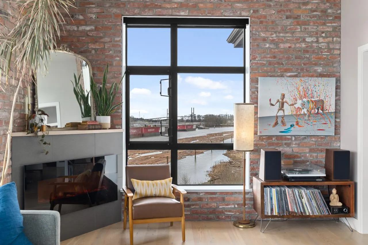 Living room with exposed brick wall, large window overlooking a river, and mid-century modern furniture.