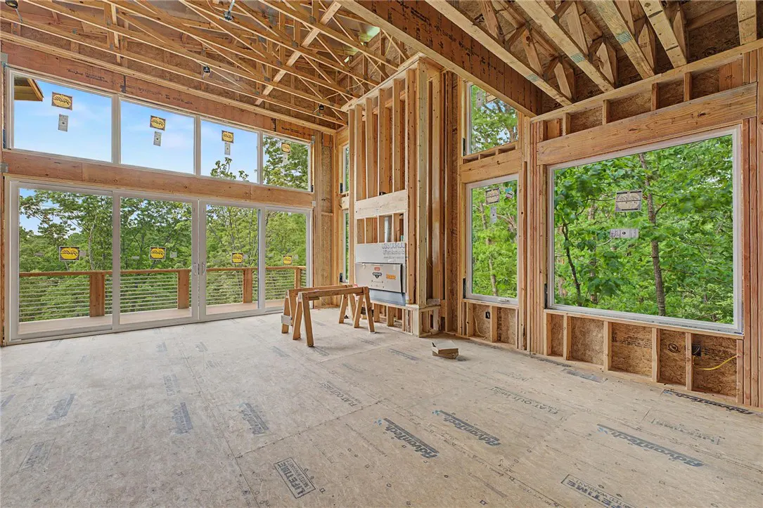Unfinished room with wood framing, large windows overlooking green trees, and a wooden floor.