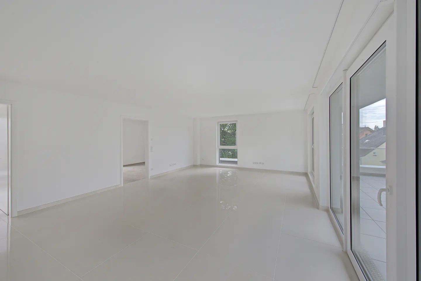 Bright, empty living room with white walls, glossy tiled floors, and large glass doors leading to a balcony.