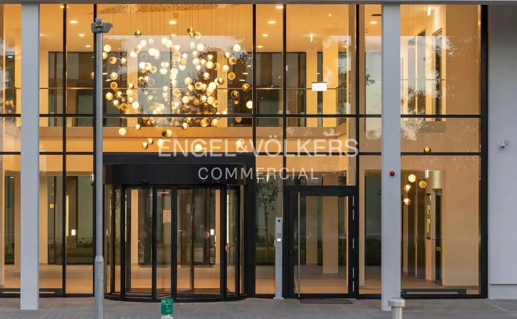 Exterior view of Engel & Völkers Commercial with a revolving door and glass windows. A modern chandelier hangs inside.