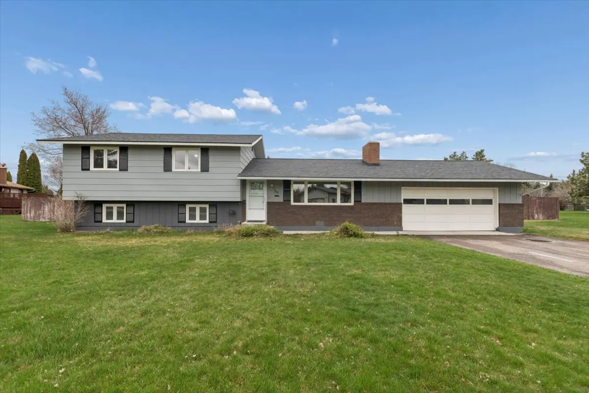 Two-story gray house with black shutters and a white garage door on a green lawn under a blue sky.