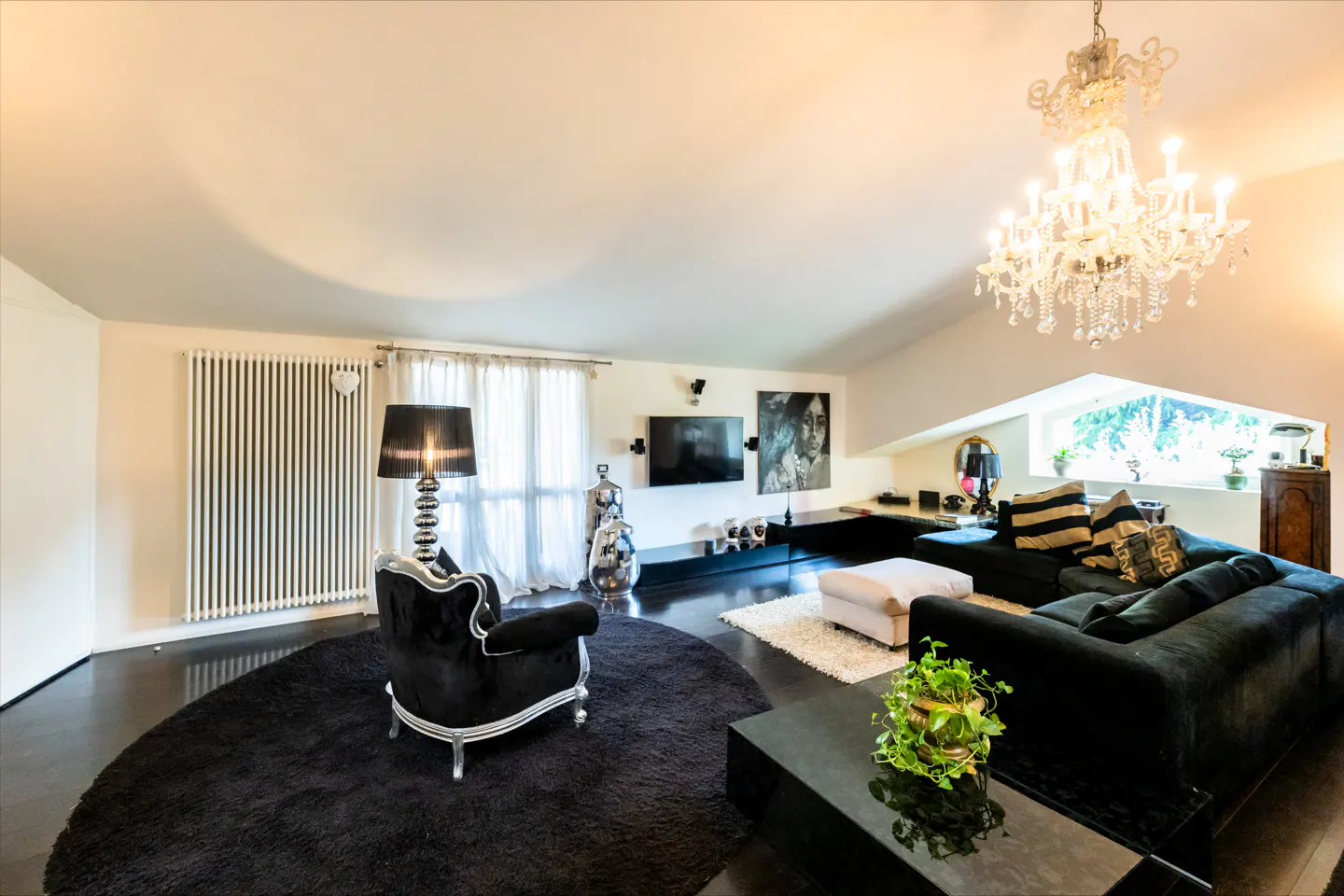 Living room with black sofa, chair, and rug. A crystal chandelier hangs from the ceiling. A TV and artwork are on the wall.