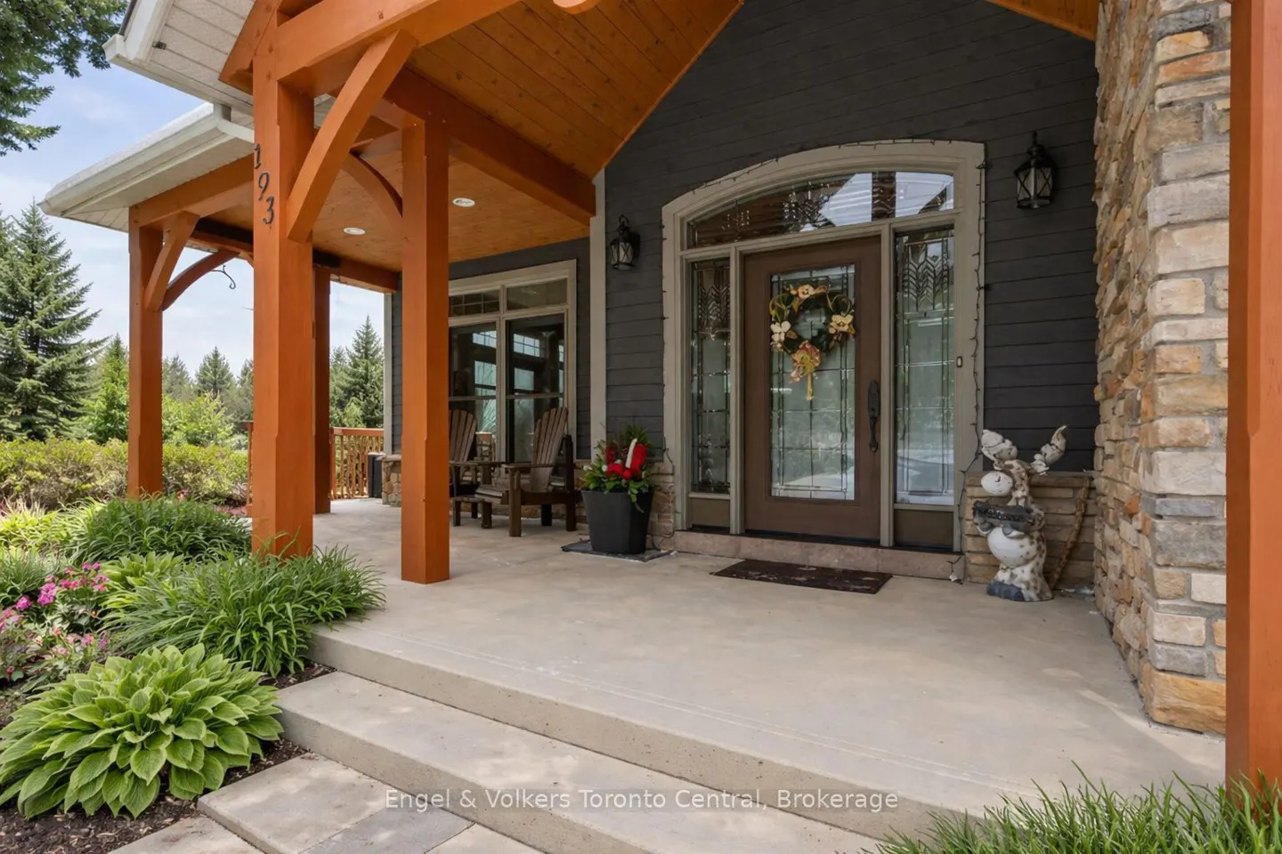 Front entrance of a house with a brown door, wreath, and wooden porch. Stone accents and green landscaping.