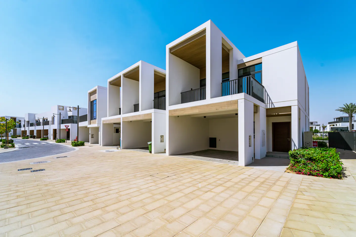 Row of modern white townhouses with open carports under a clear blue sky. Paved driveway in the foreground.