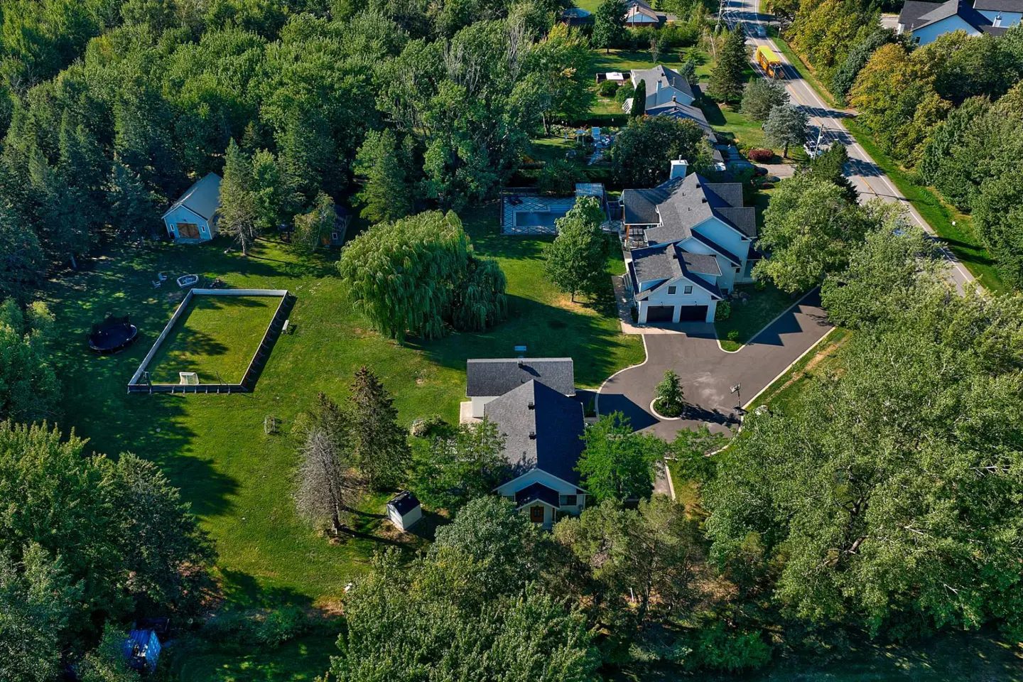 Aerial view of a large property with a house, pool, and green lawn surrounded by lush trees.