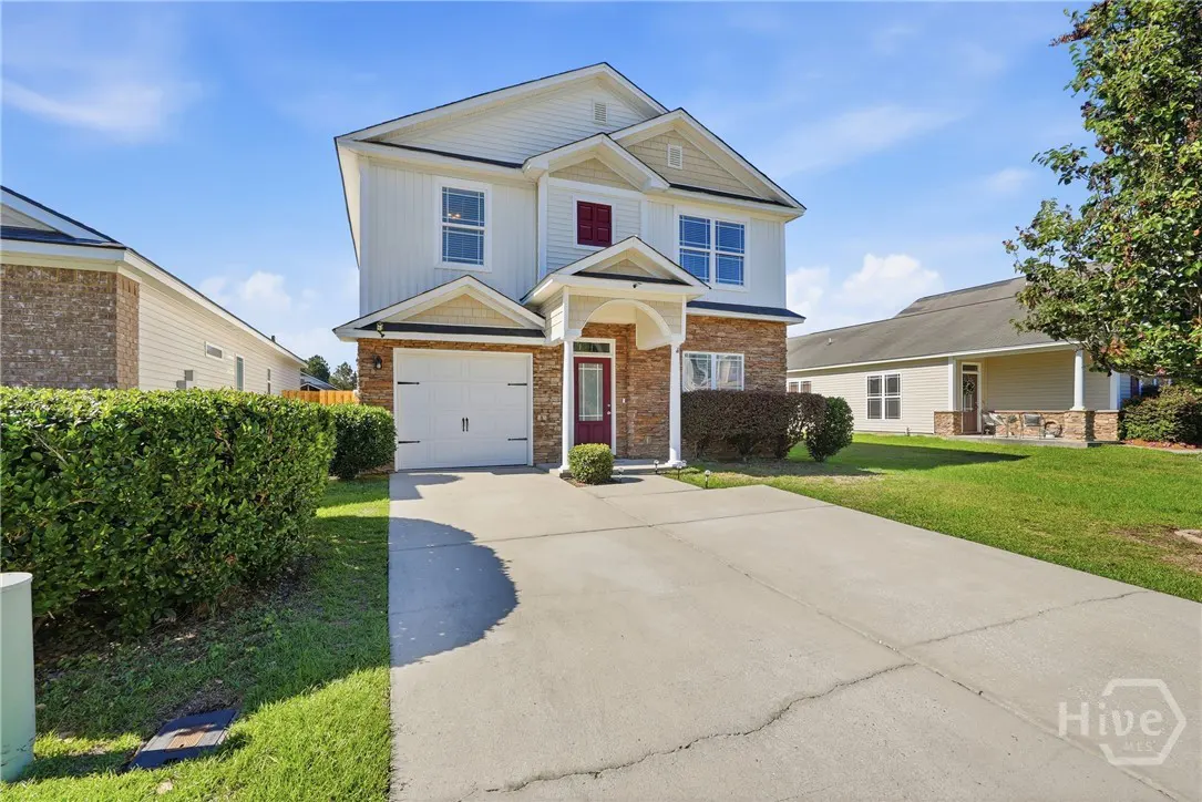 Two-story house with white siding, stone accents, red door, white garage door, and a concrete driveway. Green lawn and blue sky.