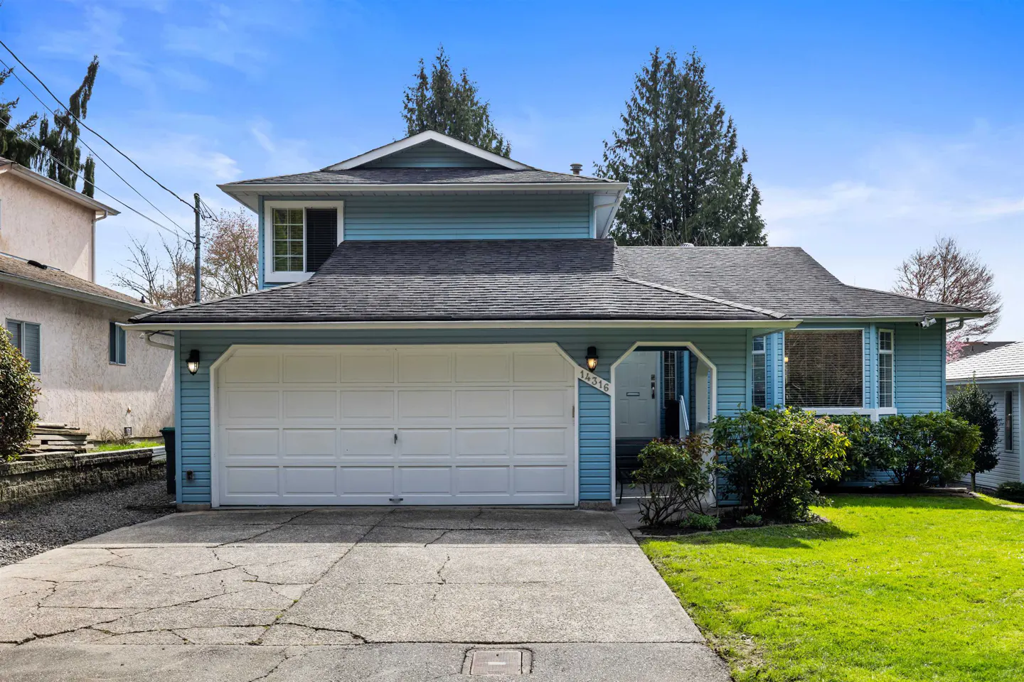 A light blue, two-story house with a white garage door and a gray roof on a sunny day.