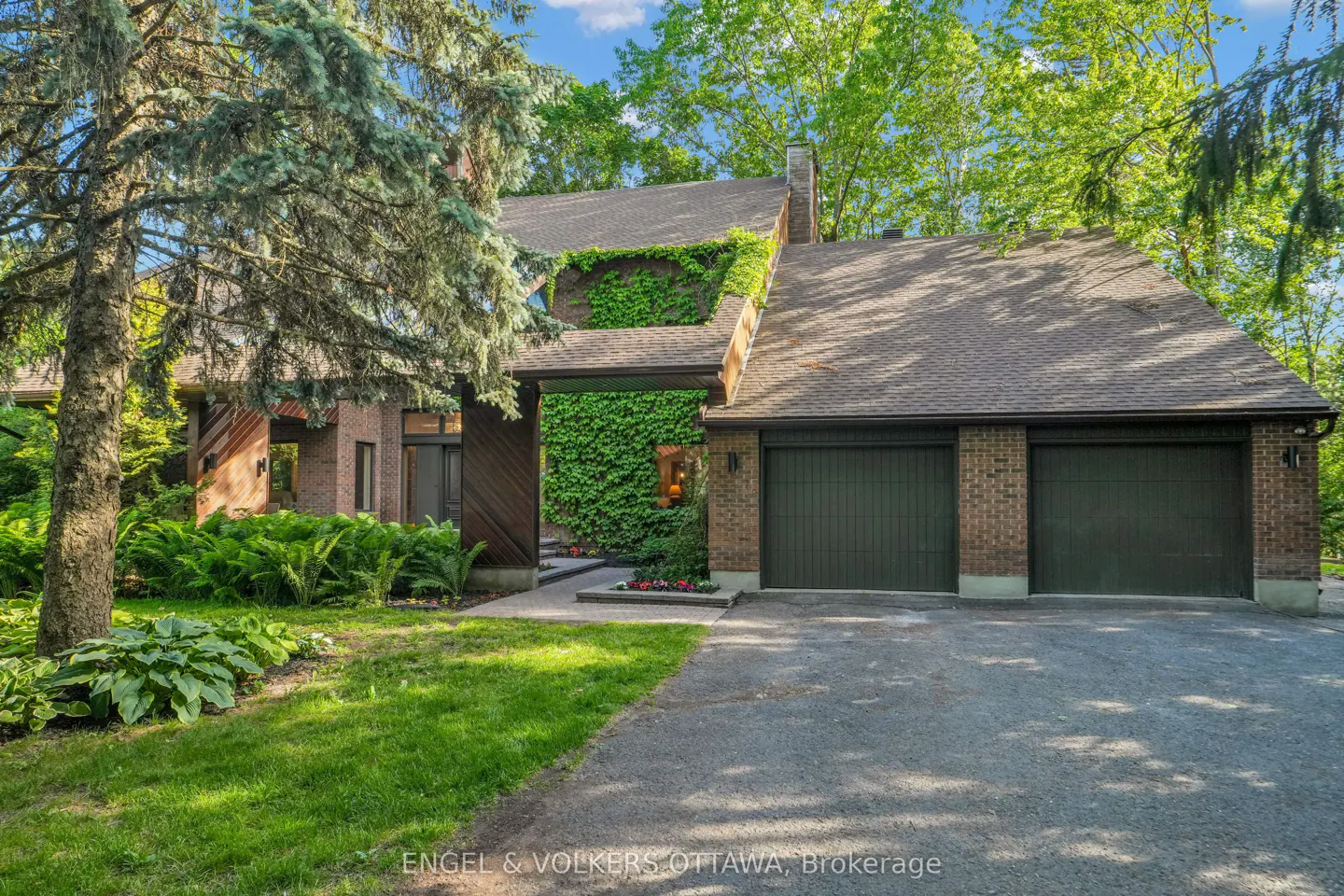 Brick house with a two-car garage, ivy-covered walls, and lush green landscaping under a bright blue sky.