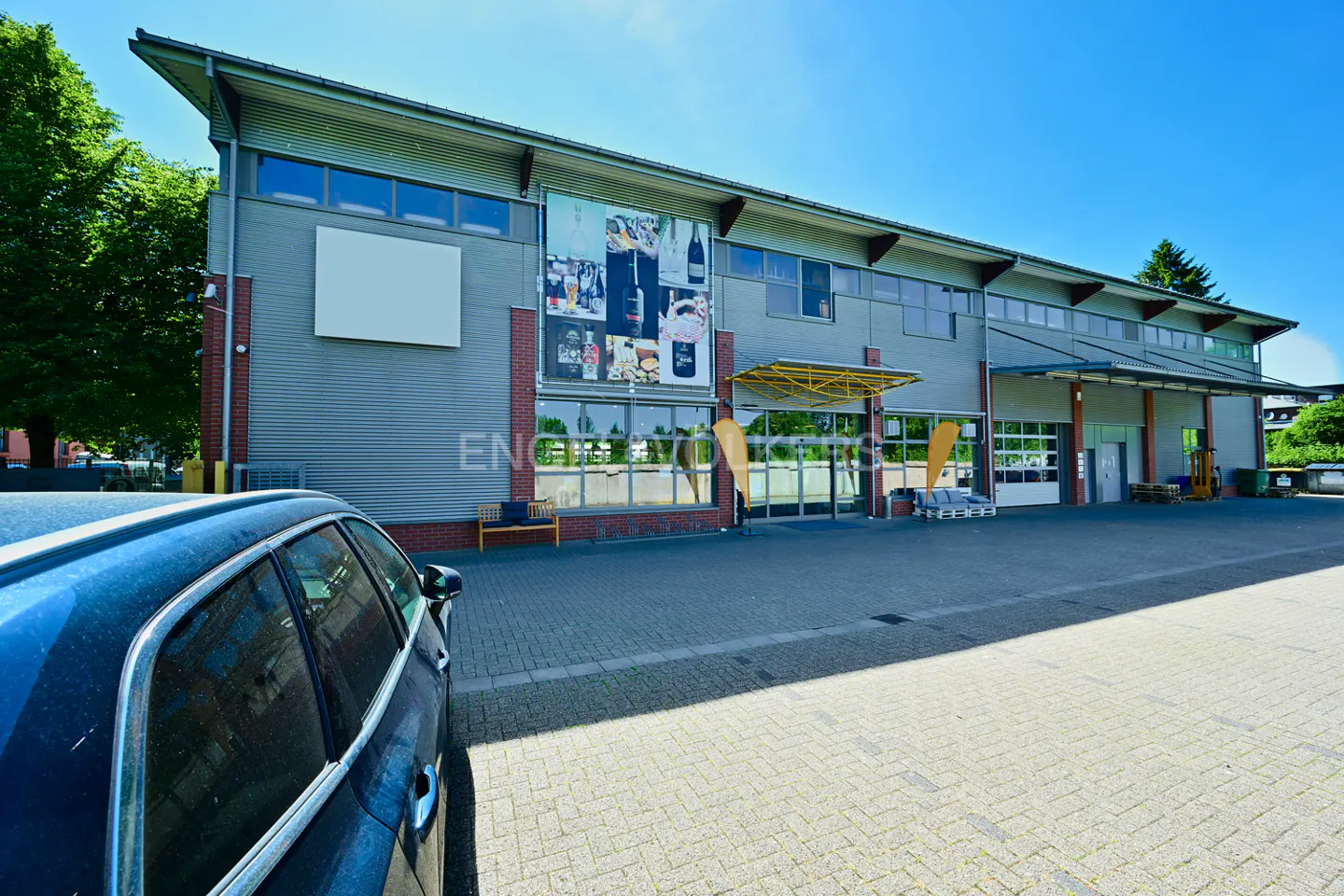 Exterior of a gray commercial building with a large advertisement and a blue car in the foreground.
