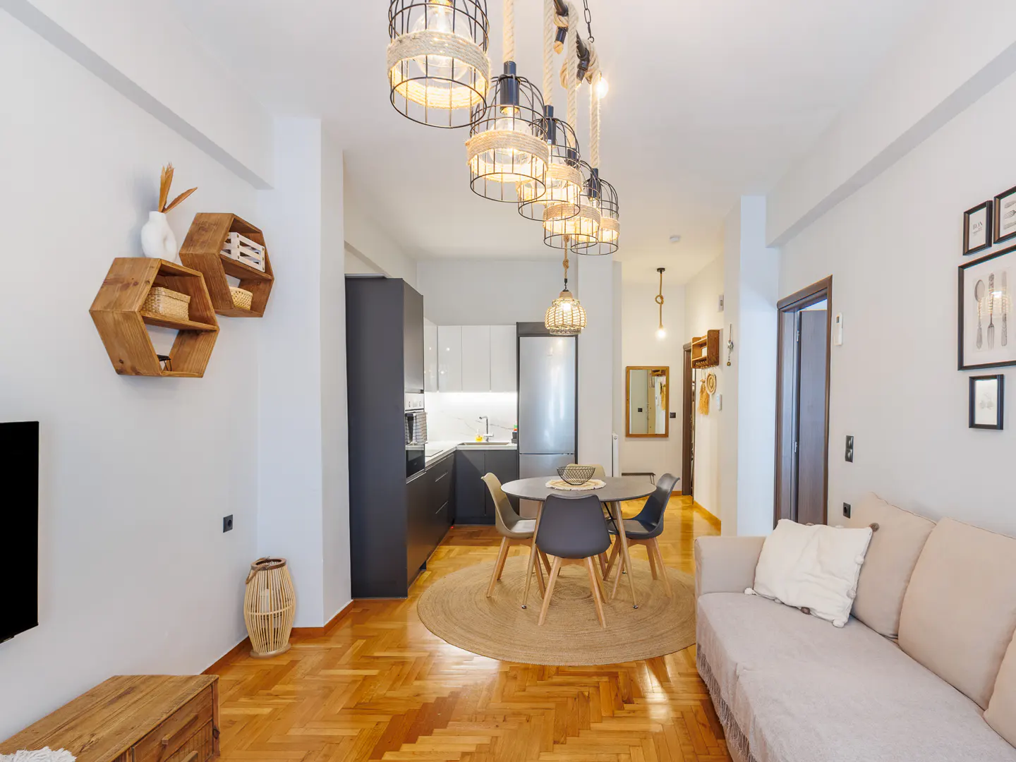 Bright apartment interior with wood floors, white walls, and modern decor. Kitchen, dining area, and living room are visible.
