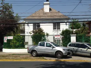 Two-story white house with a brown roof and chimney, green fence, and two parked cars.