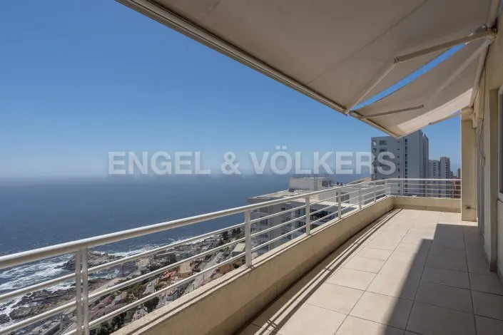 Balcony view of the ocean with white railings, beige tile floor, and a retractable awning above. Engel & Völkers logo visible.