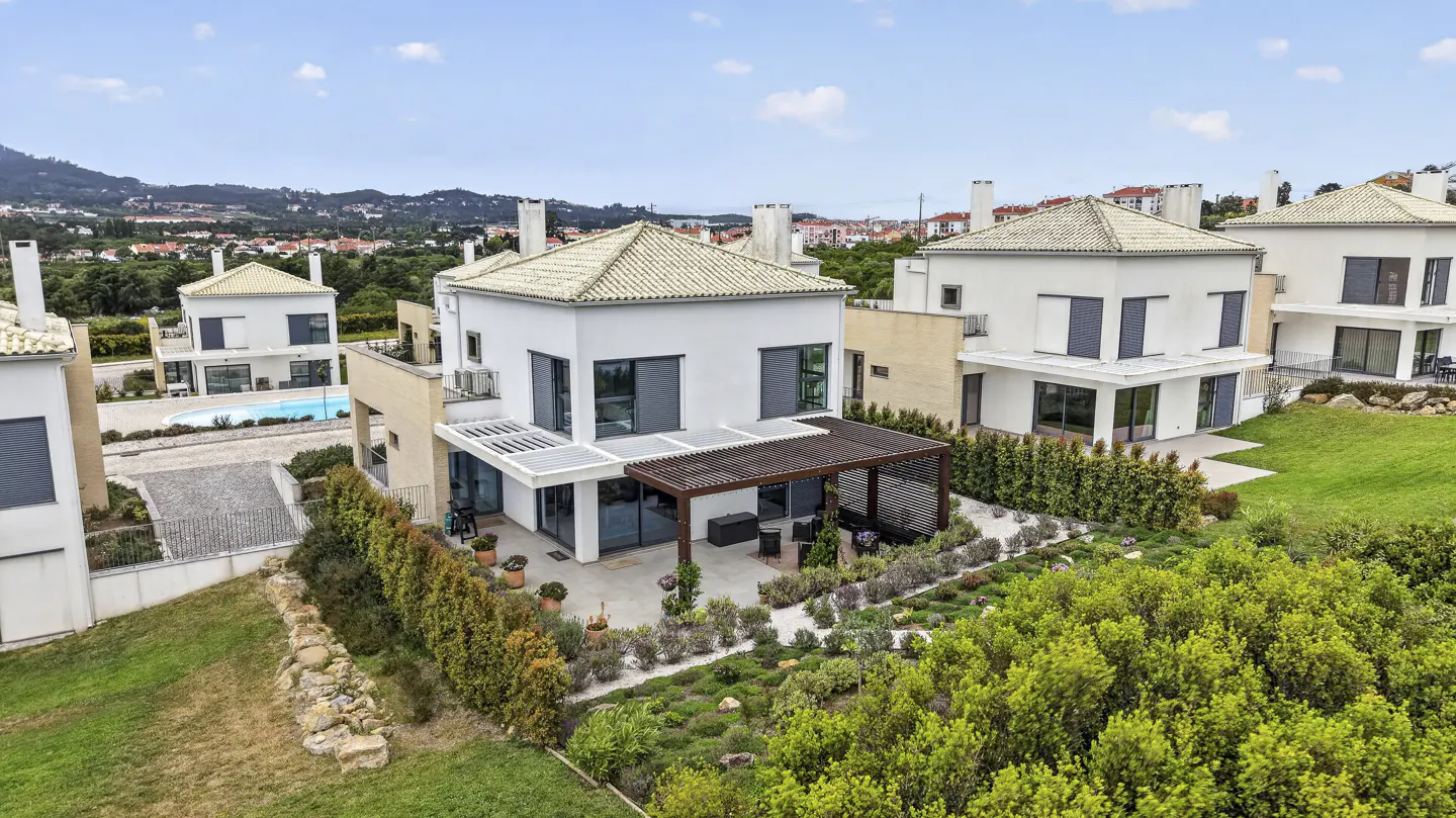Aerial view of modern white houses with tile roofs, patios, and green landscaping on a sunny day.