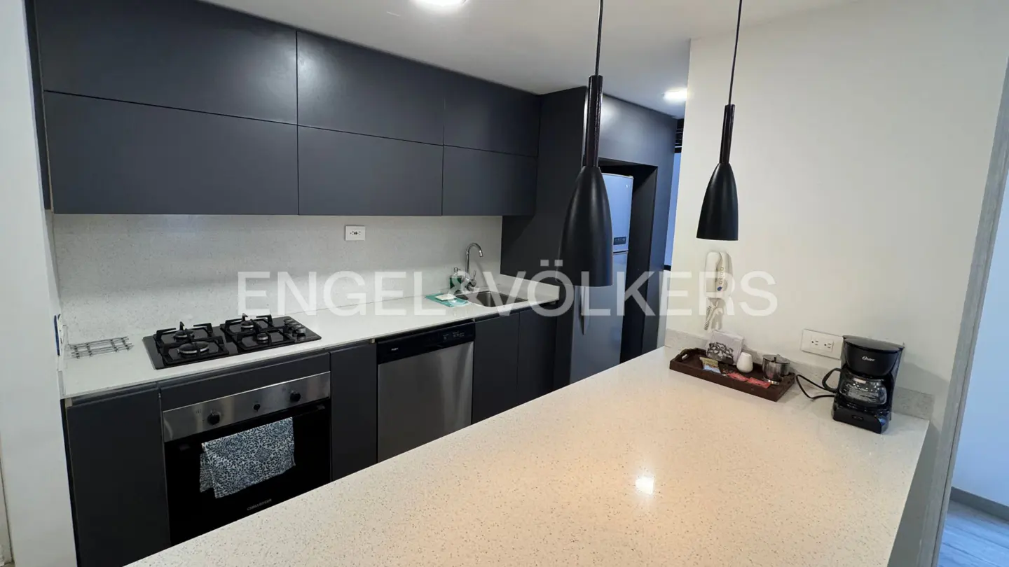 A modern kitchen with gray cabinets, stainless steel appliances, and a white countertop. Two black pendant lights hang above the counter.