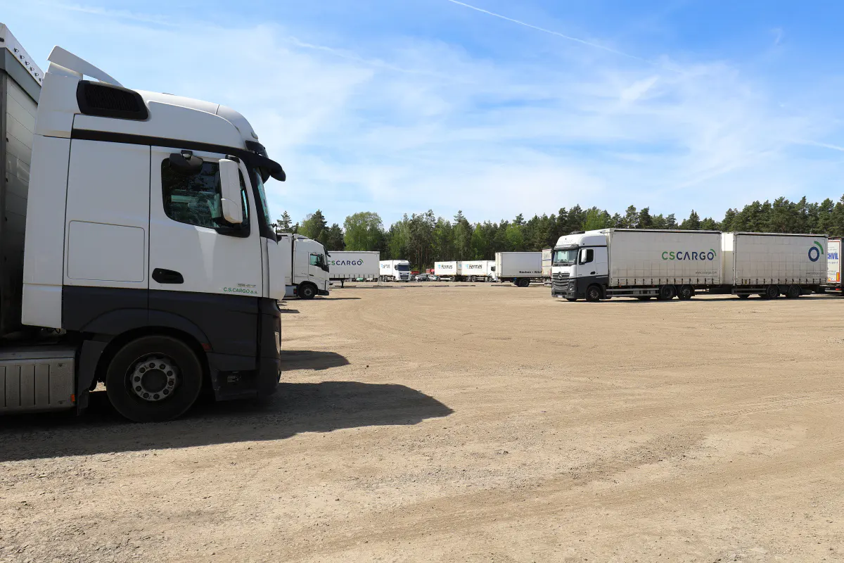 A large, dirt parking lot filled with white CS Cargo semi-trucks under a blue, partly cloudy sky.