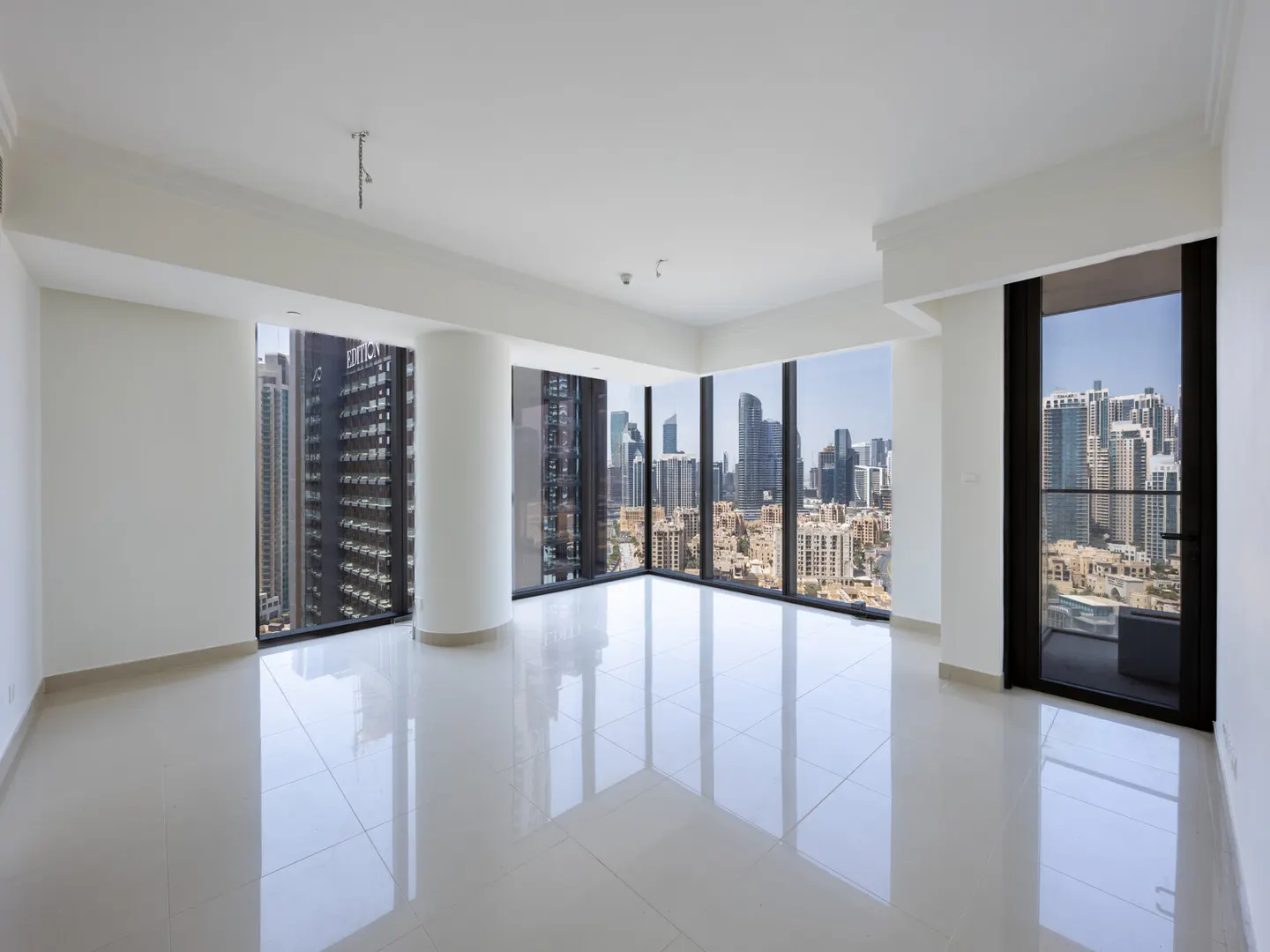 Bright, empty room with white walls, tile floor, and large windows. A city skyline is visible through the windows.