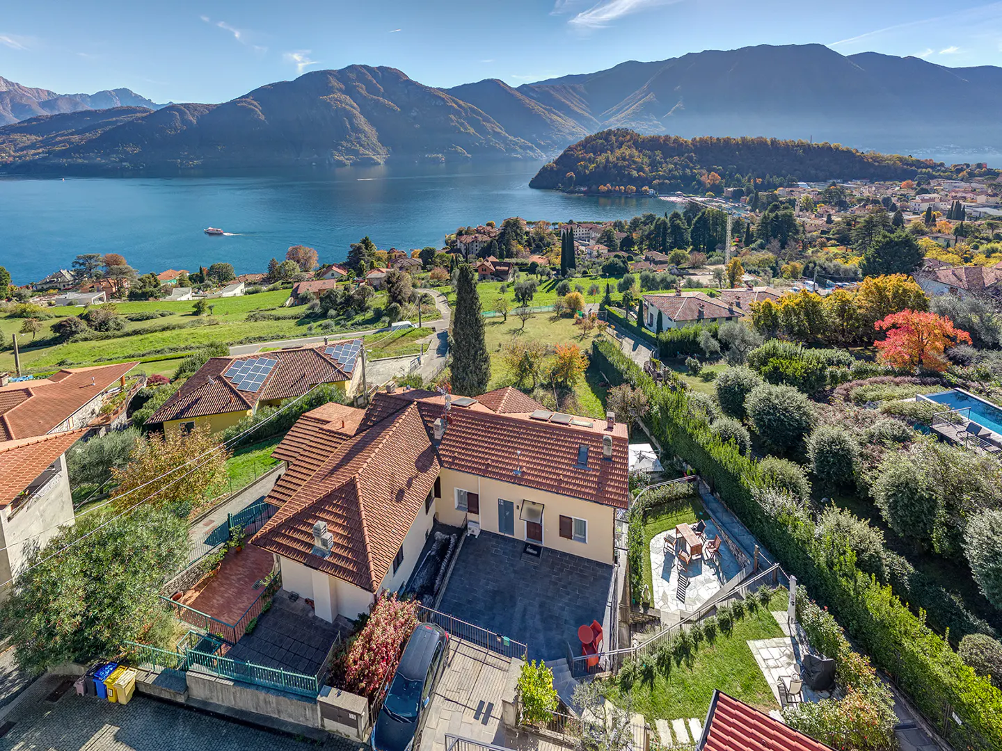 Aerial view of a yellow house with a red tile roof, a patio, and a lake and mountains in the background.