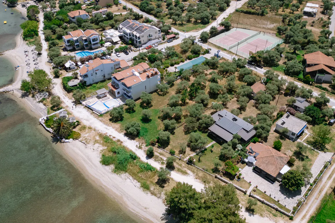 Aerial view of a coastal real estate property with houses, pools, tennis courts, and beach access.