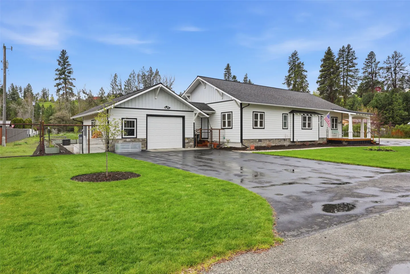 Exterior view of a white house with a black roof, a garage, and a green lawn under a blue sky.