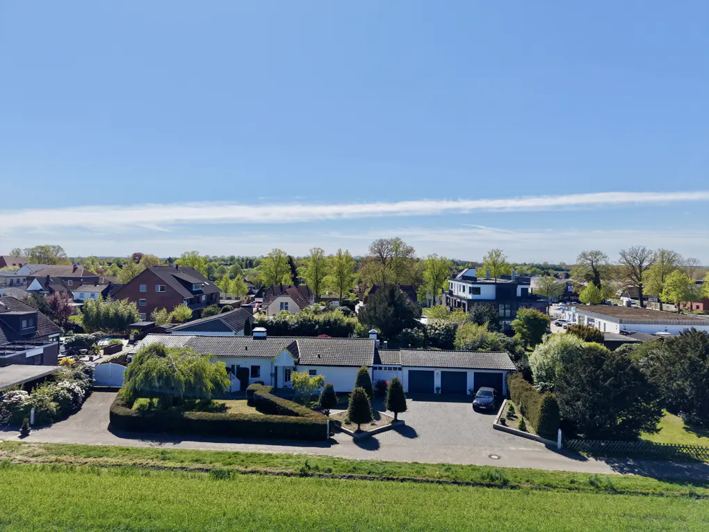 Aerial view of a white, single-story house with a three-car garage, green lawn, and blue sky.