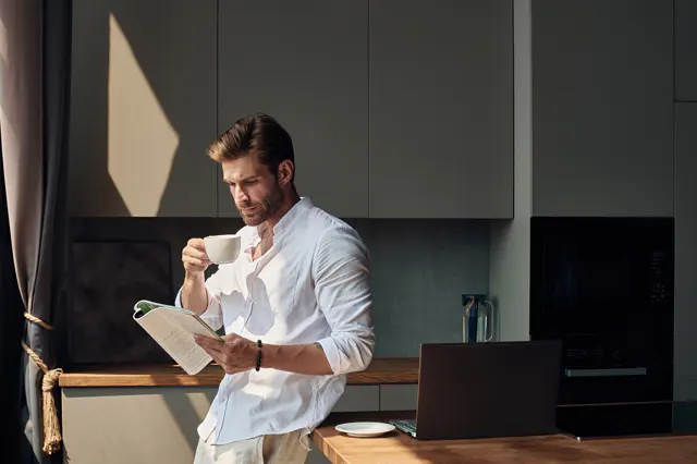 Person reading a magazine at home while holding a cup of coffee