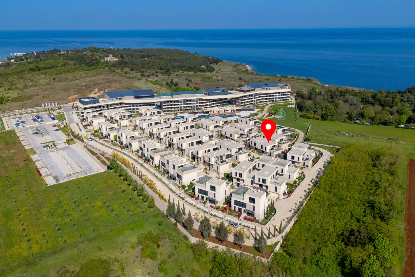 Aerial view of modern white villas near the sea, with a red pin marking a specific property.