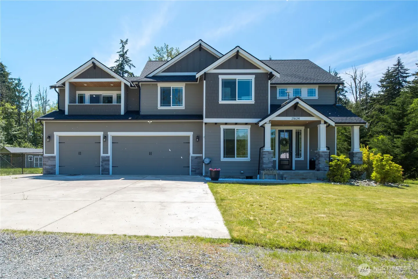 Two-story house with gray siding, white trim, and a two-car garage. Green lawn and trees surround the property.