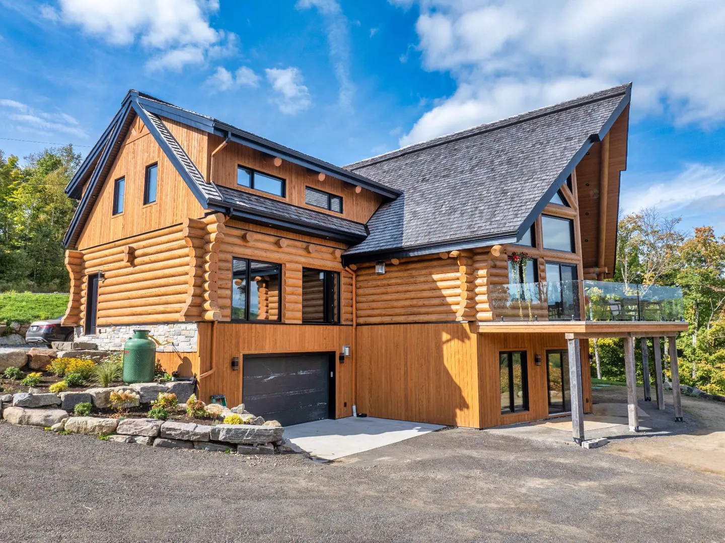 Exterior of a two-story log cabin home with a gray roof, black trim, and a deck with glass railings.