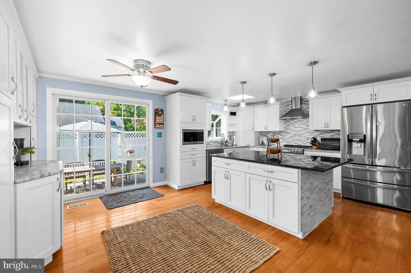 Bright kitchen with white cabinets, stainless steel appliances, and a black granite island. A sliding glass door leads to a patio.