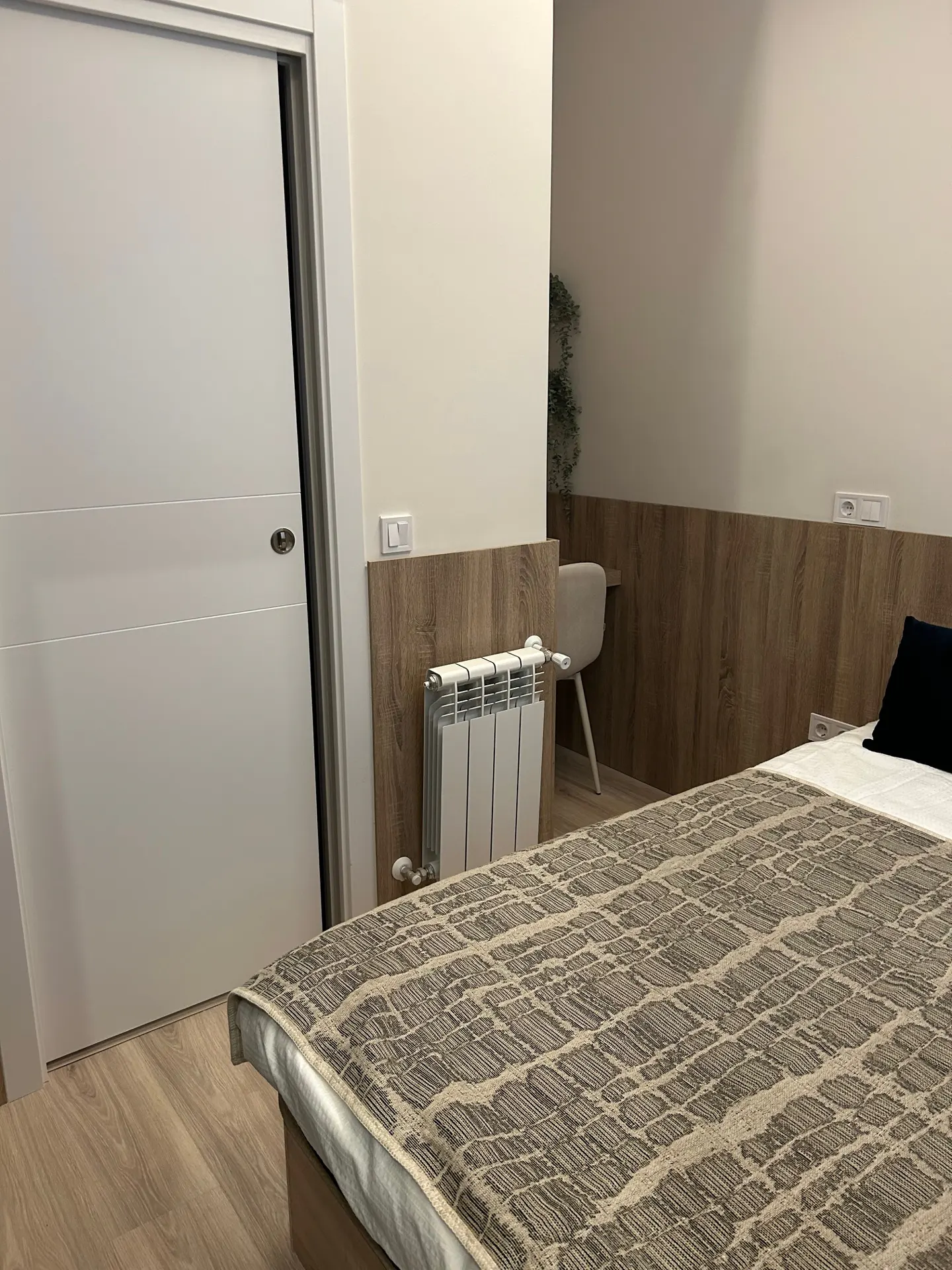 Bedroom with a bed covered in a brown patterned blanket, a white door, and a small desk with a chair.