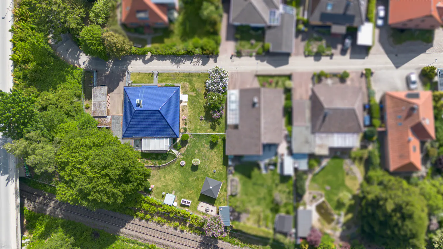 Aerial view of a house with a bright blue roof, large green yard, and nearby train tracks in a suburban neighborhood.