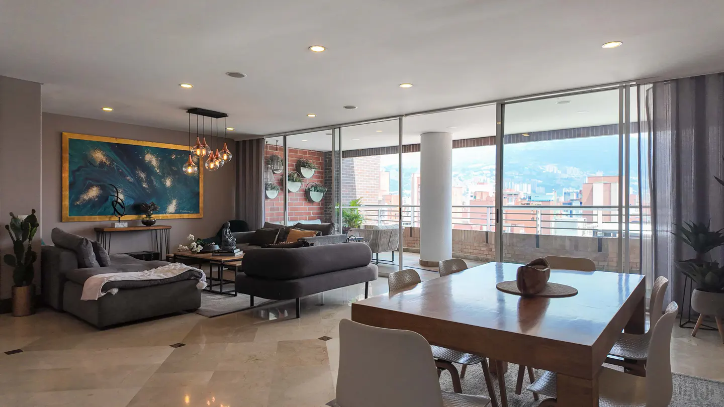 Open-concept living and dining area with gray sofas, wood table, and city view through large windows.