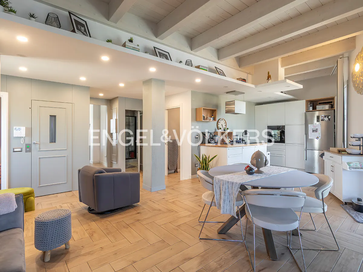Modern open-plan living area with light wood floors, a grey armchair, and a dining table with white chairs near a kitchen.