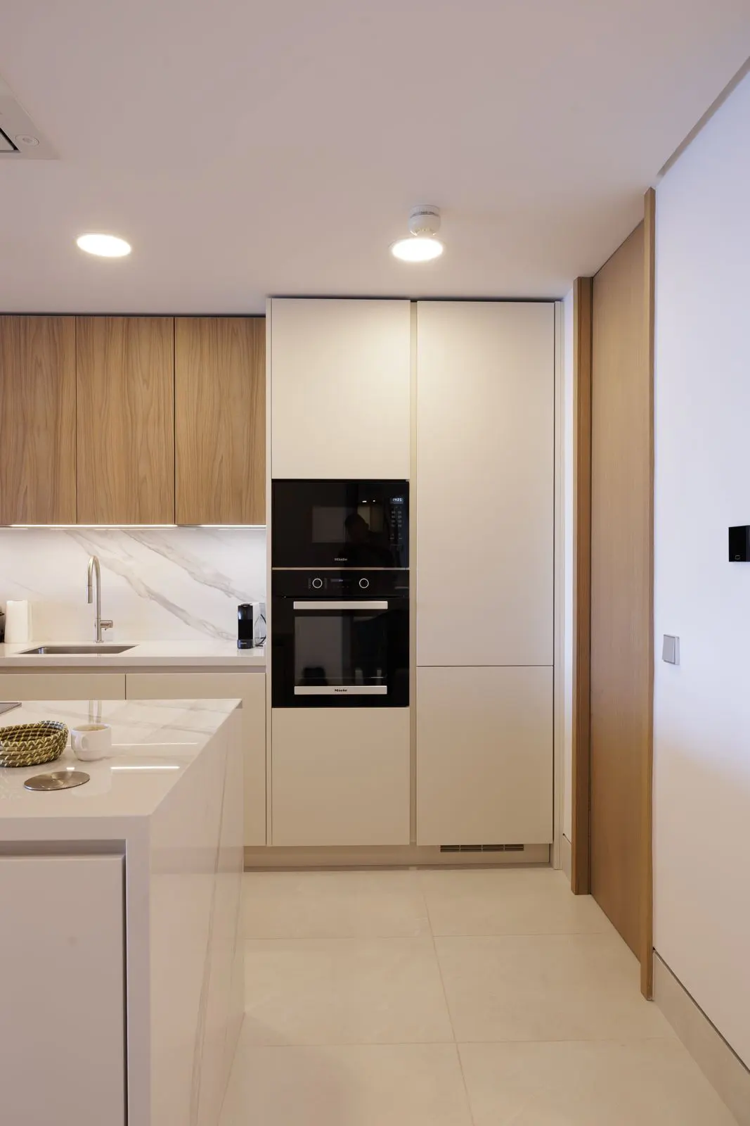 A modern kitchen with light wood cabinets, white countertops, and stainless steel appliances.