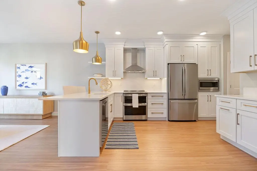 Bright, modern kitchen with white cabinets, stainless steel appliances, and gold pendant lights over an island with a gold faucet.