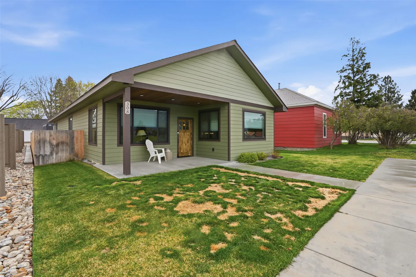 Exterior of a one-story, light green house with a brown roof and trim, a small porch, and a green lawn.