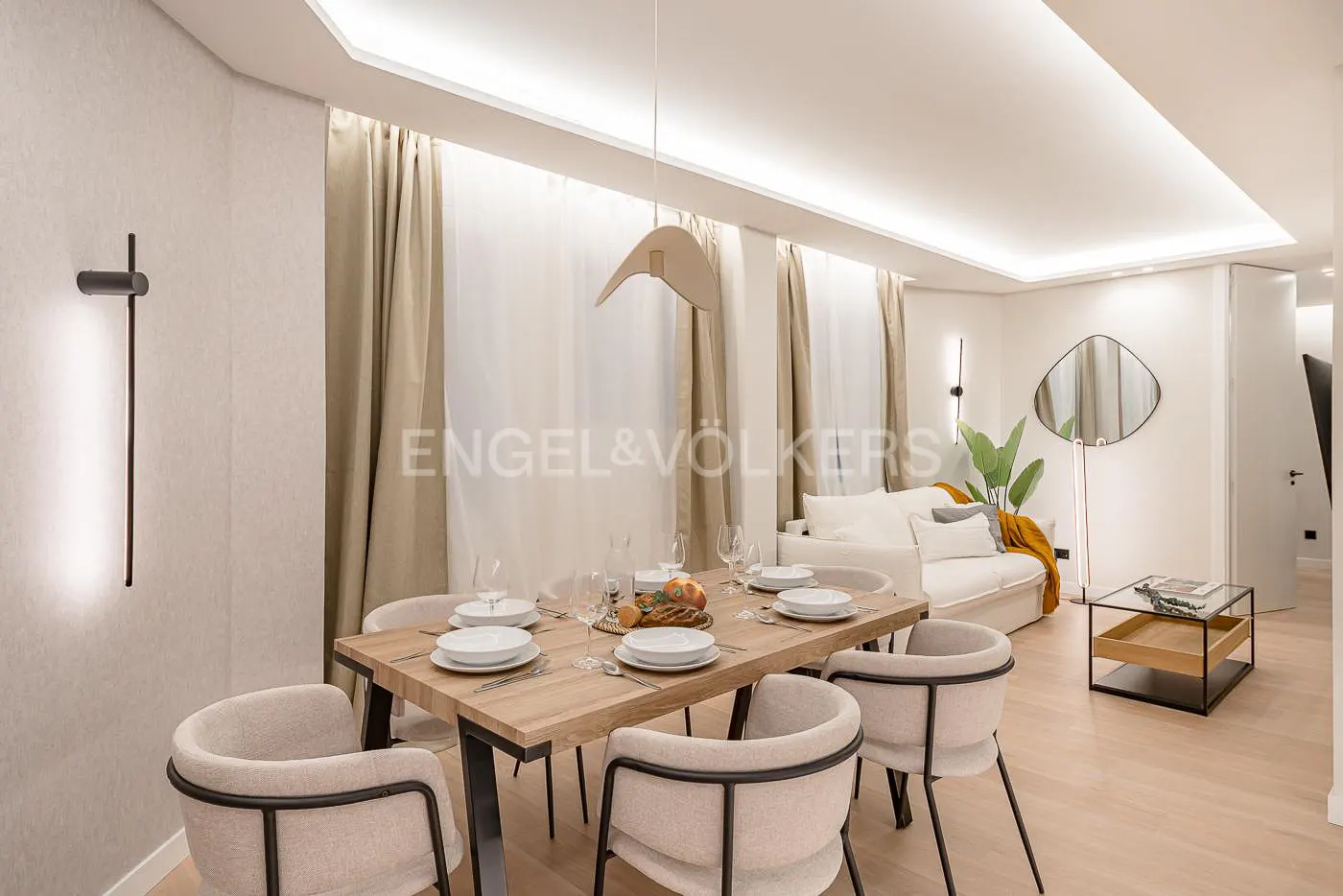 Bright, modern living and dining area with a wood table set for six, a white sofa, and neutral decor.