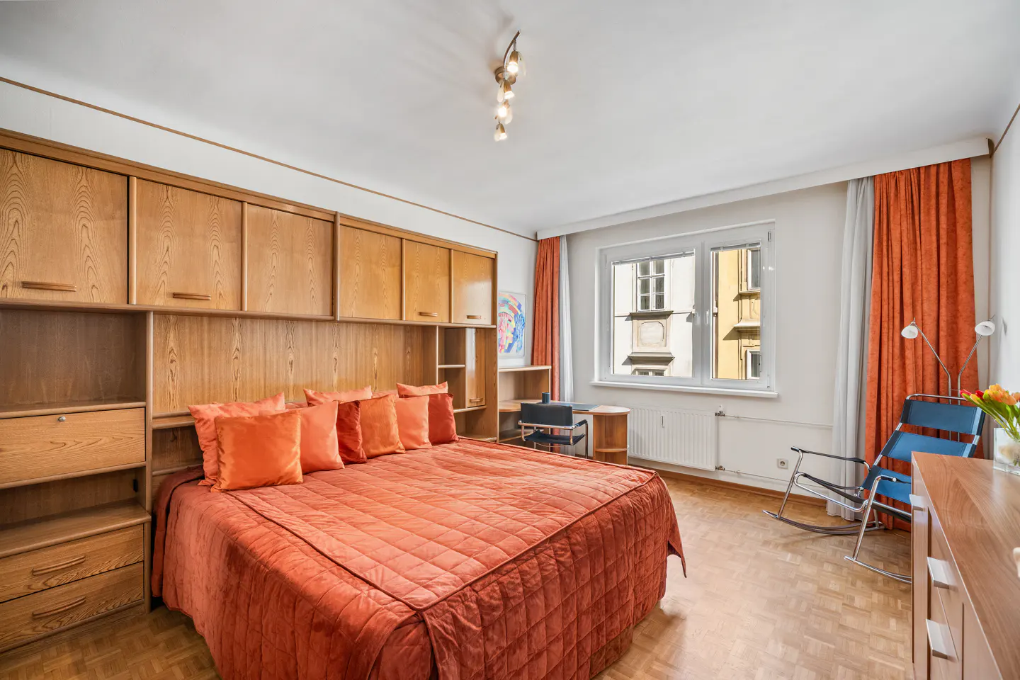 Bedroom with orange bedding, wood built-ins, and a window view of a building.