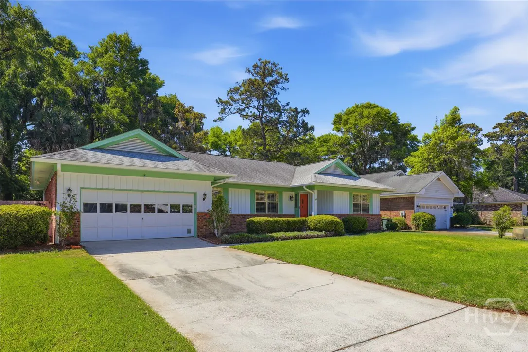 A ranch-style house with a green trim, white siding, and an orange front door. A driveway leads to a two-car garage.