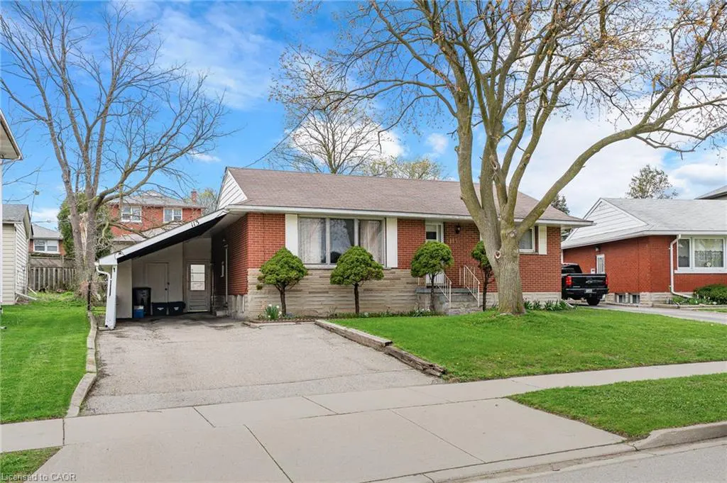 A red brick bungalow with a brown roof, a carport, and a green lawn on a sunny day.