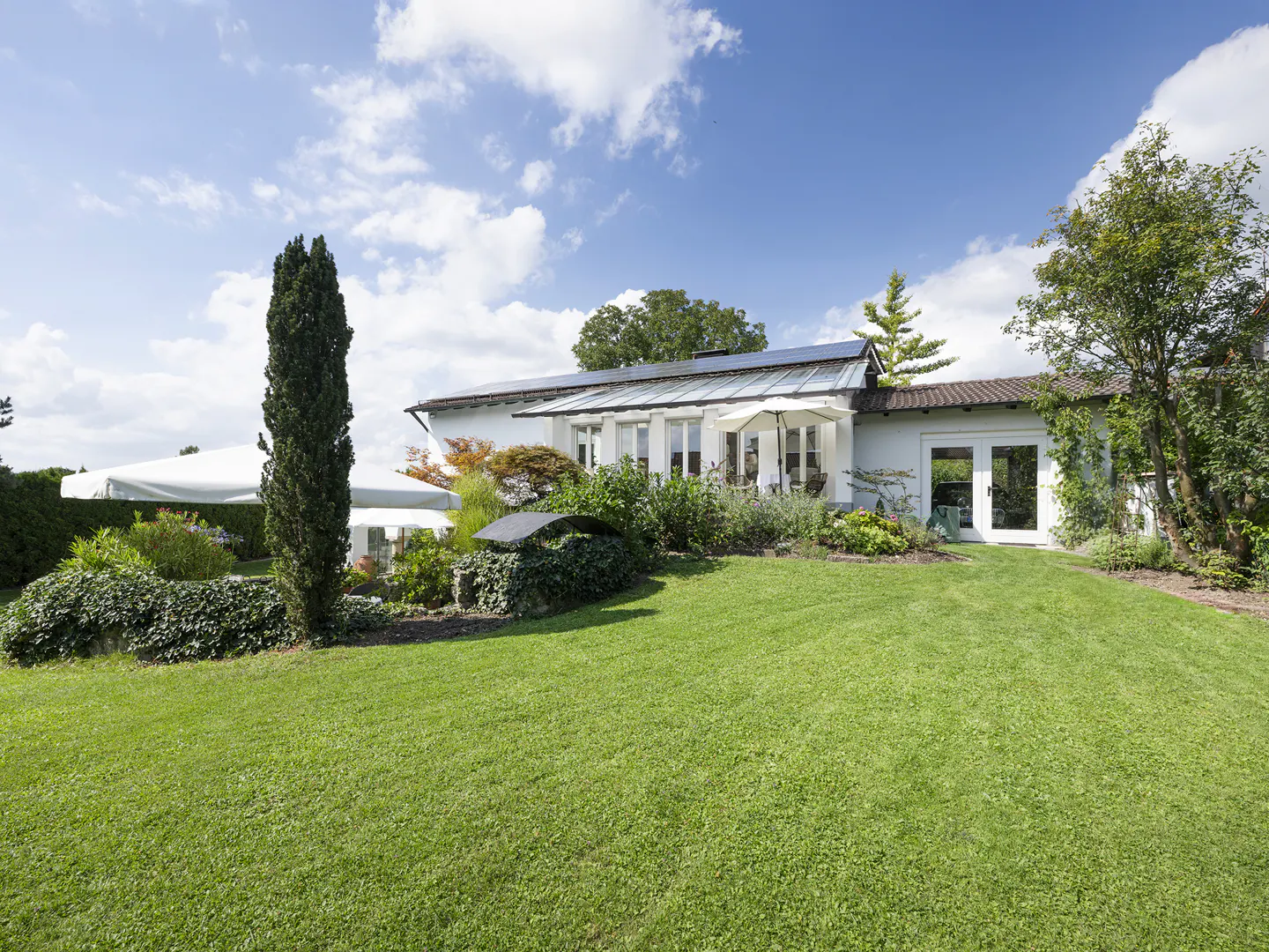 A white house with a green lawn and blue sky. Solar panels are on the roof.