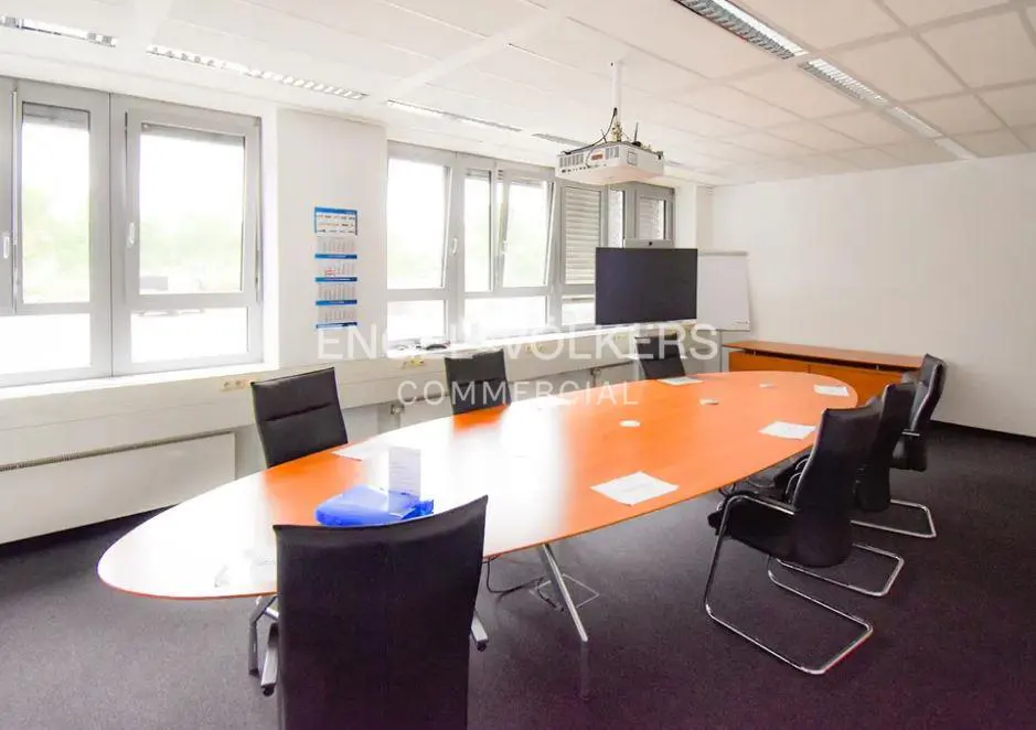 Bright office conference room with an orange oval table, black chairs, projector, and large windows.