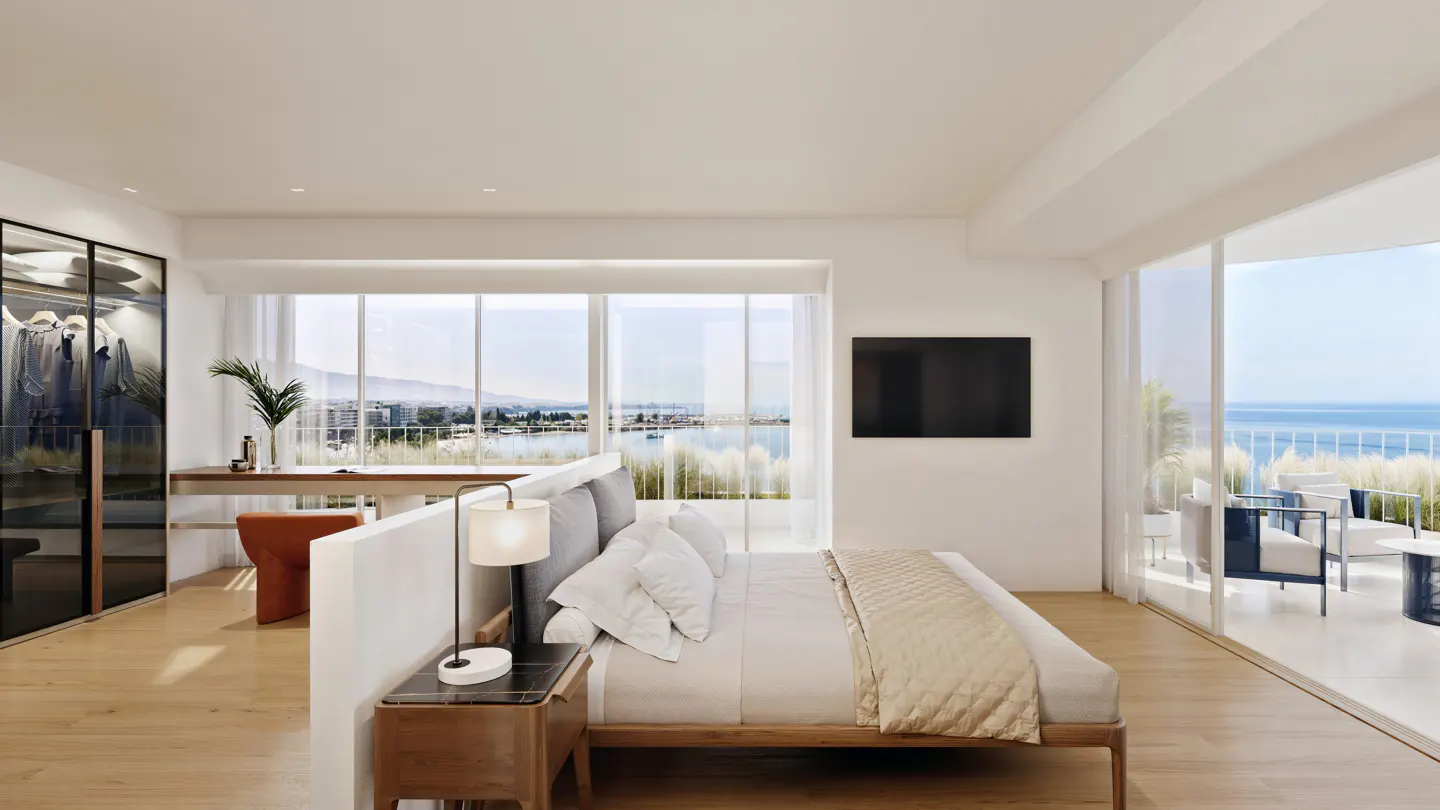Bright bedroom with a wood floor, a bed, a desk, and a closet. A balcony overlooks the ocean.