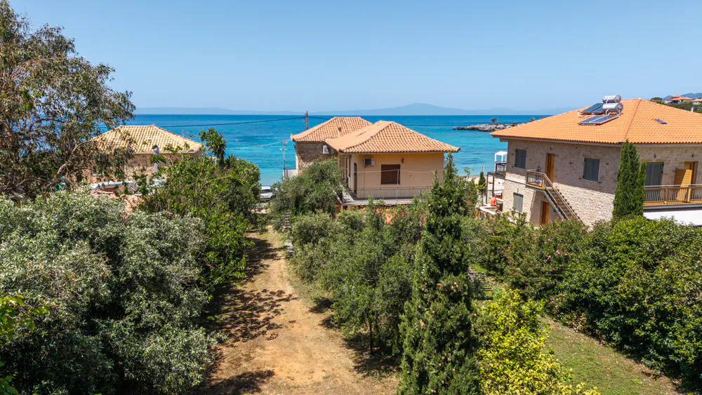 View of houses with orange tile roofs, green trees, and blue ocean in the background on a sunny day.