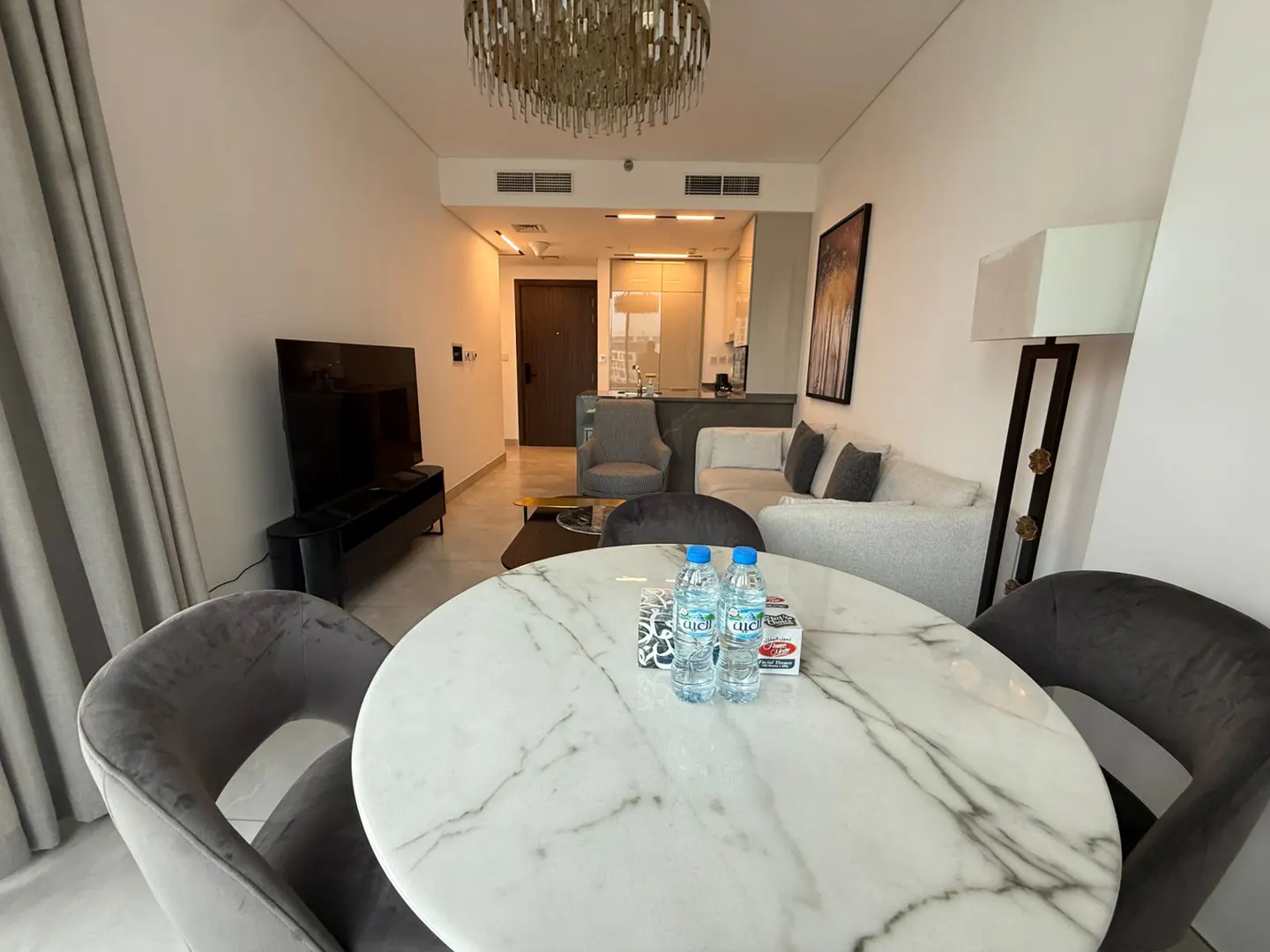 A modern apartment interior with a marble table, grey chairs, and a view of the living room and kitchen.