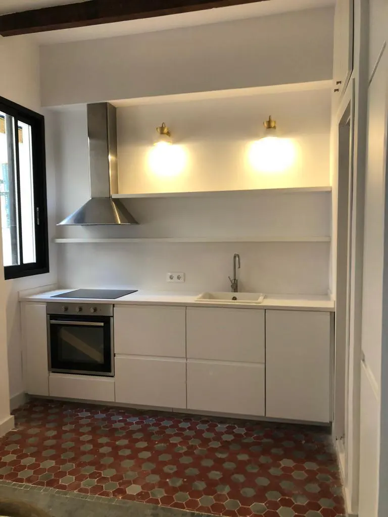 Bright kitchen with white cabinets, stainless steel hood, and red hexagonal tile floor. A black-framed window is on the left.