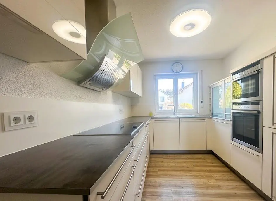 Bright kitchen with white cabinets, dark countertops, and wood floors. A window provides natural light. Stainless steel appliances are visible.