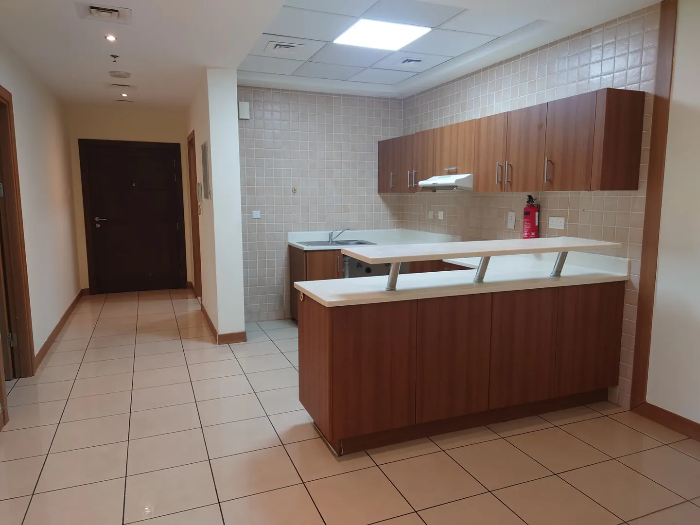 Kitchen with wood cabinets, white countertops, and a breakfast bar, set against light tiled walls and floors.